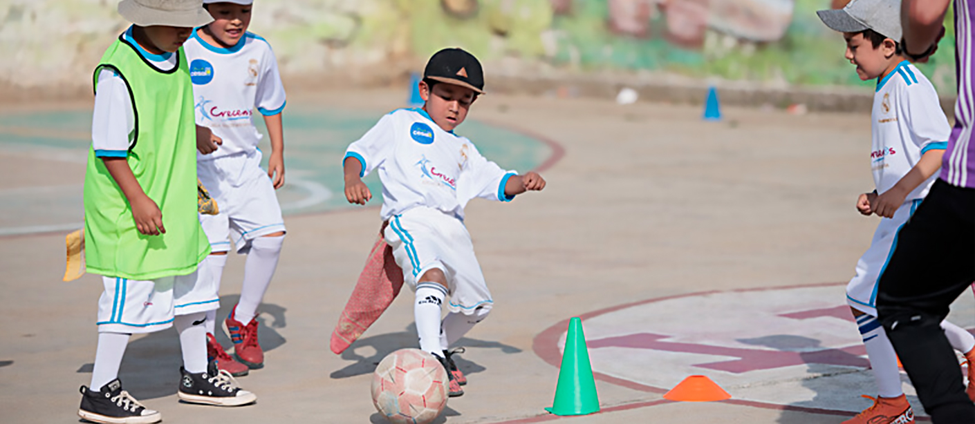 A child surrounded by three other kids and an adult coach kicks a soccer ball.